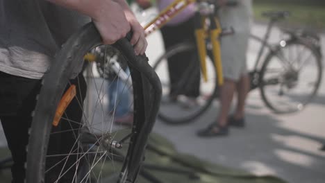 un mecánico de bicicletas inserta un nuevo tubo en una rueda de bicicleta con otra bicicleta y un mecánico en el fondo