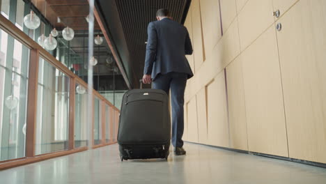 an unrecognizable businessman walks backwards with a trolley