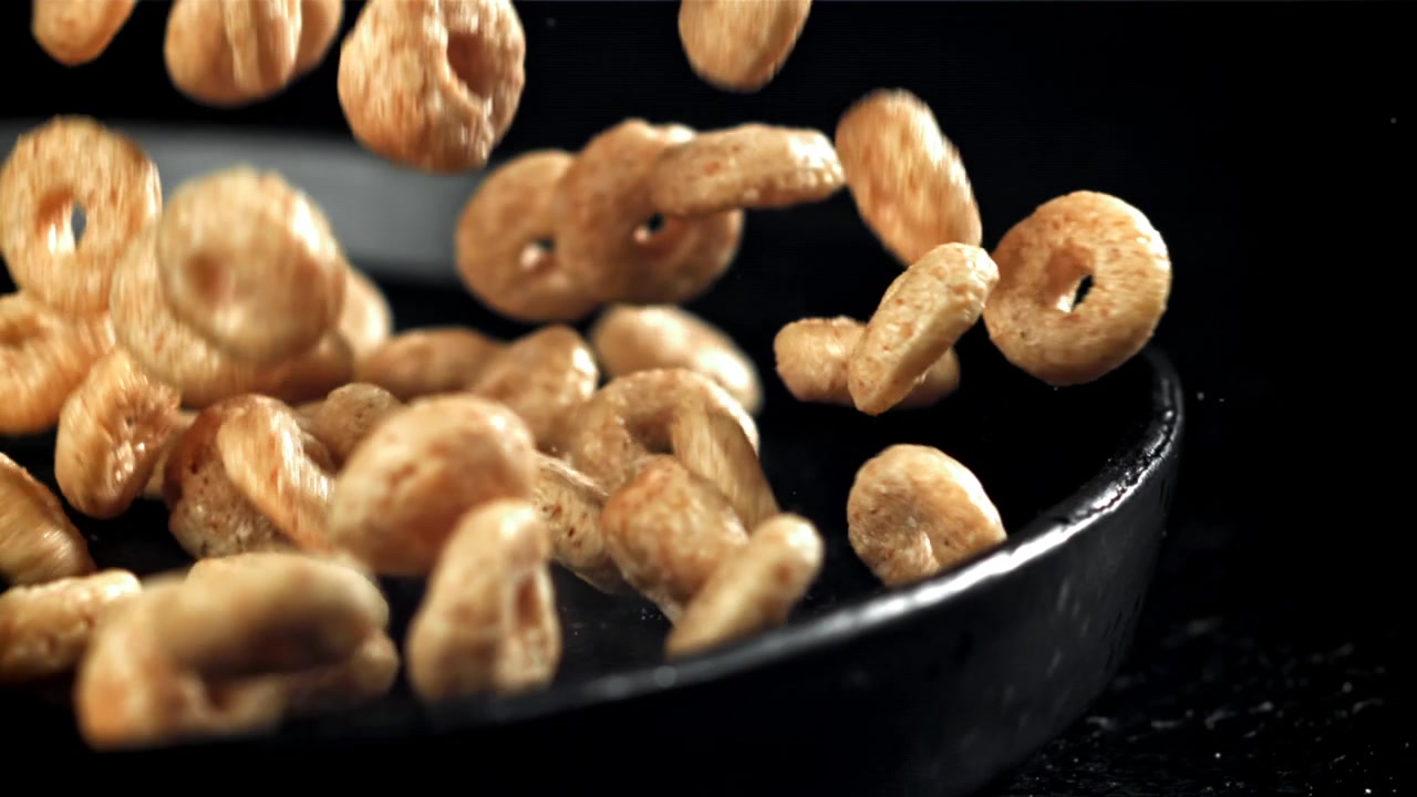 Golden Cereal Rings Pouring into a Dark Bowl in Slow Motion