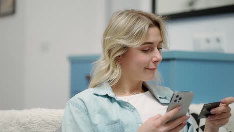 Happy-young-woman-holding-black-credit-card-using-instant-mobile-payments-at-home