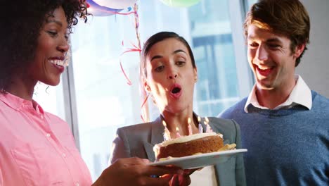 mujer de negocios soplando velas de cumpleaños con colegas