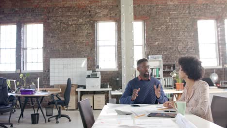 Diverse-architect-colleagues-discussing-work-at-table-with-blueprint-in-slow-motion