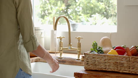 washing hands at kitchen sink with fresh vegetables in basket nearby, at home