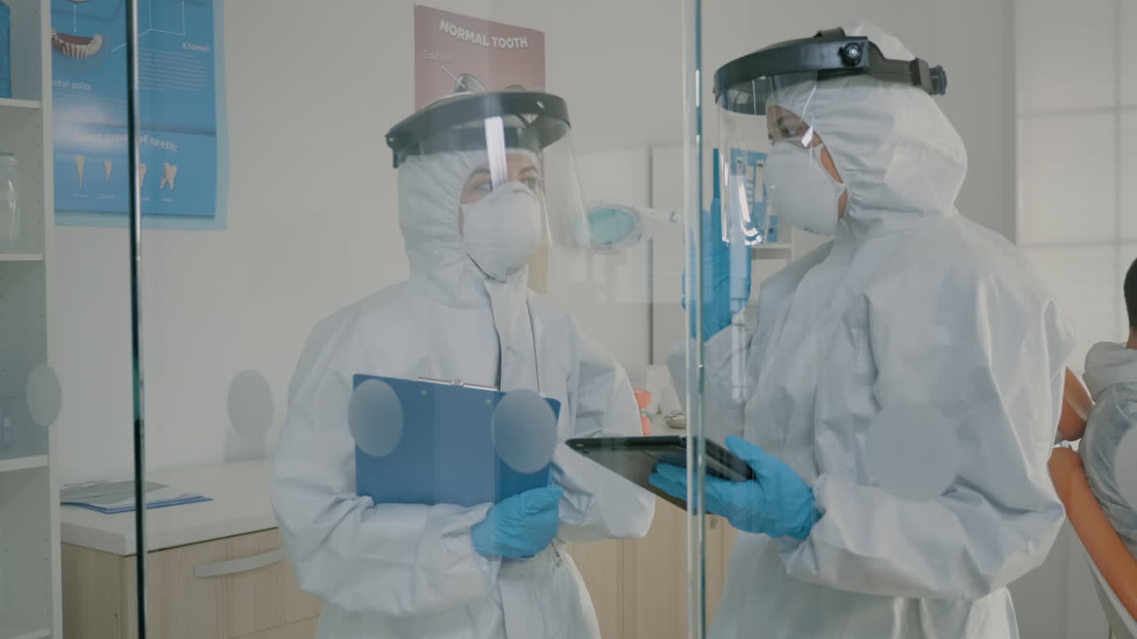 치아 위생용 태블릿을 사용하는 하즈마트 슈트를 입은 치과 의사