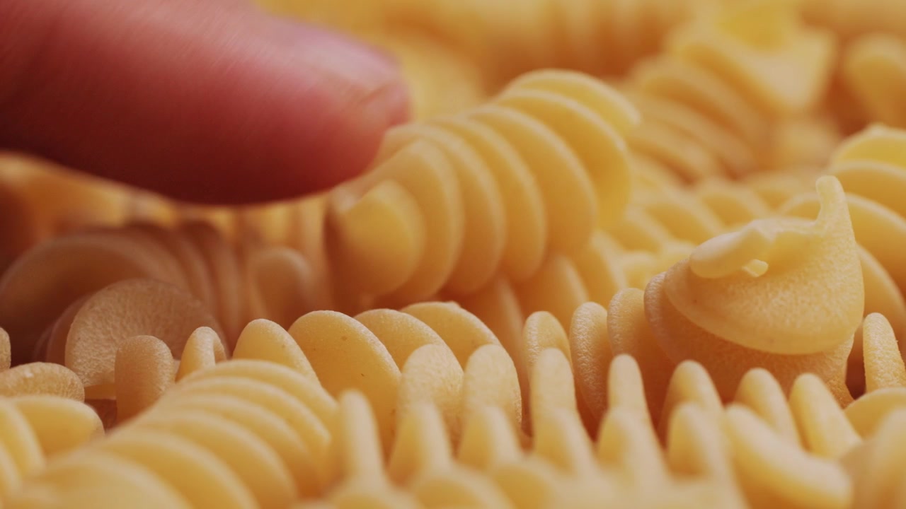 Close-up of a Hand Touching Uncooked Fusilli Pasta