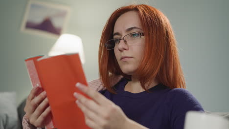 redhead housewife in glasses reads interesting short novel