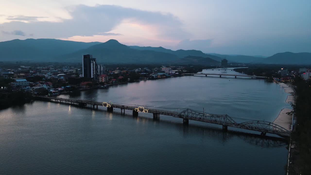 Several scooters ride over the narrow historic Entanou bridge with four-litre lighting with beautiful reflection in the calm Preaek Tuek Chhu river. wide panning shot