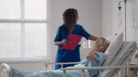 a dark-skinned female doctor is talking to an old male patient lying on a hospital bed discussing rehabilitation after recovery.