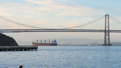 ship passing oakland bay bridge at dawn