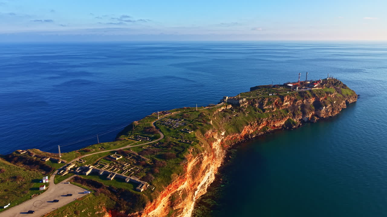Isola con scogliere rocciose, vegetazione ed edifici vicino all'acqua al tramonto, con cielo terso e orizzonte lontano