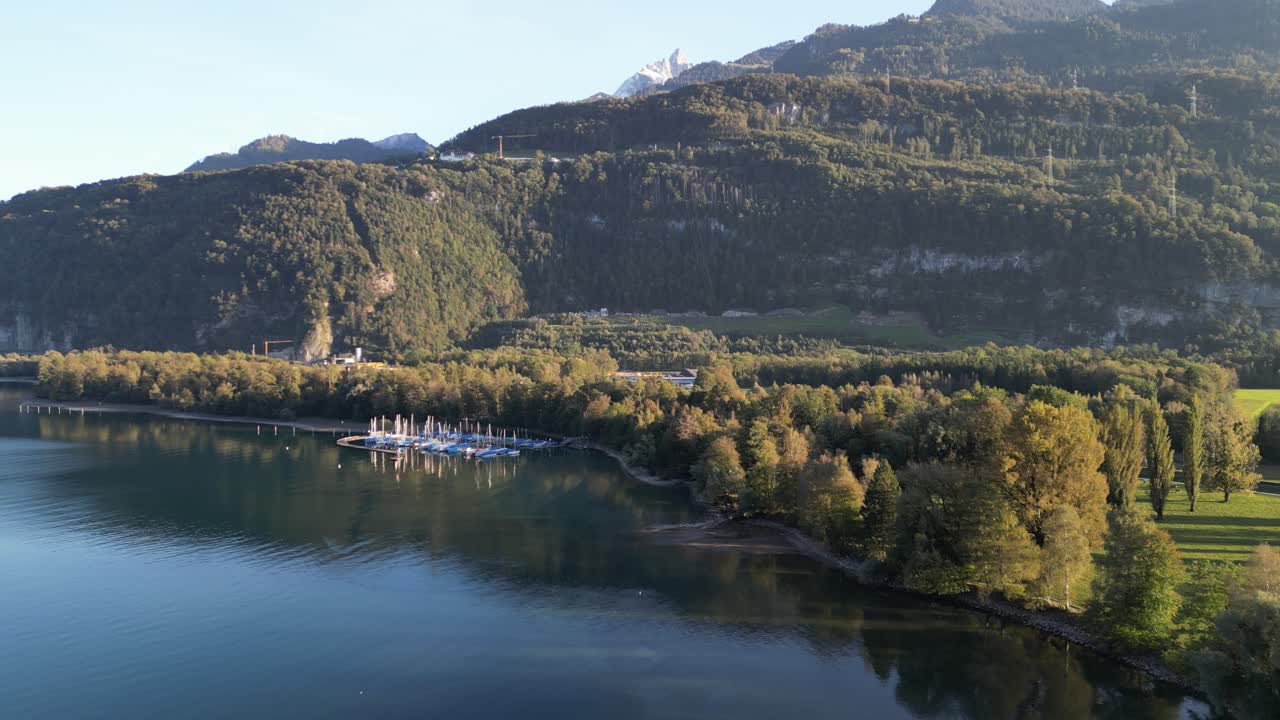 una vista serena del lago walensee con veleros atracados en un pequeño puerto deportivo y árboles empapados de sol en las colinas de la montaña