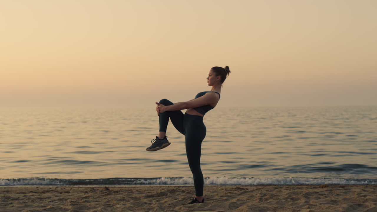 Sporty girl holding knee stretching legs on beach. Sportswoman warming up feet.