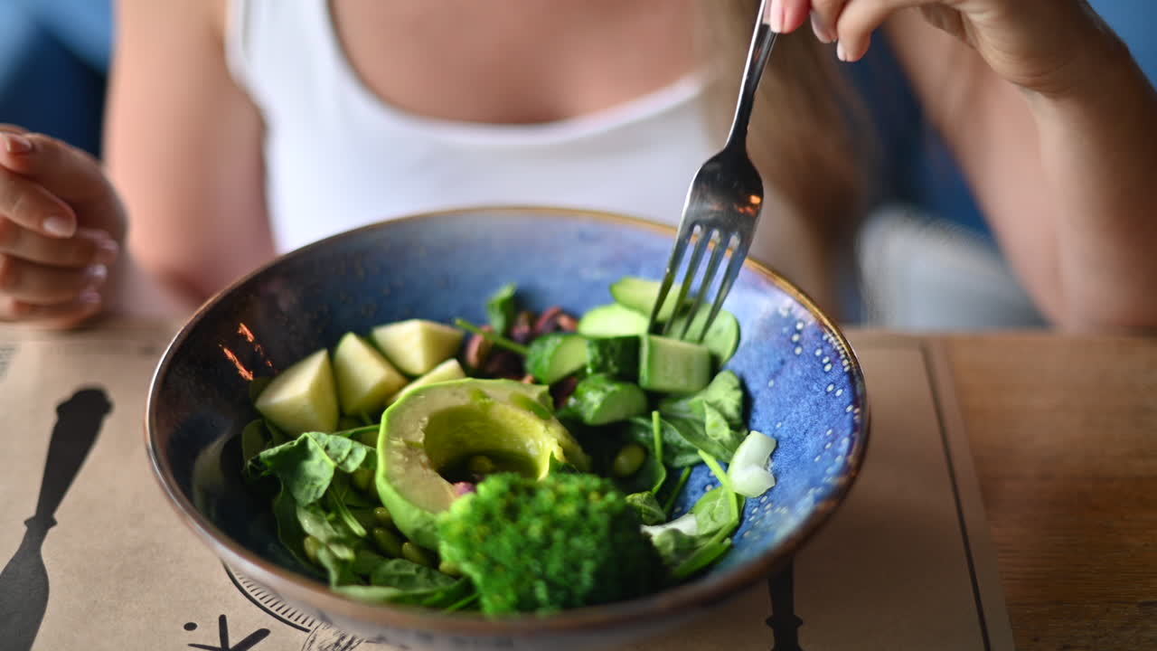 Mulher morena comendo uma salada verde em um restaurante