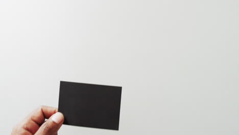 mano de hombre biracial con tarjeta de visita negra en fondo blanco, espacio de copia, cámara lenta