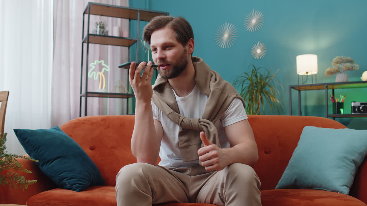 Lykkelig spent ung mann som har telefonsamtale snakker med venn som sitter og ringer i sofaen hjemme