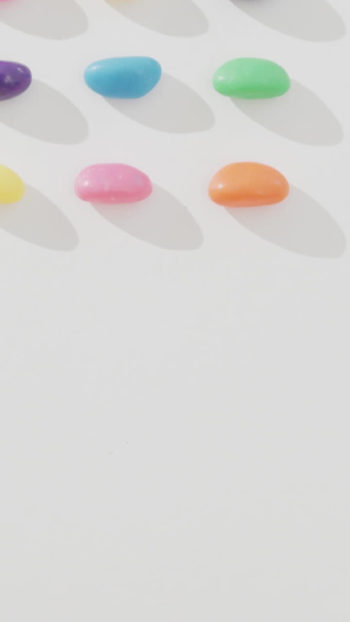 Video of overhead view of rows of multi coloured sweets over white background