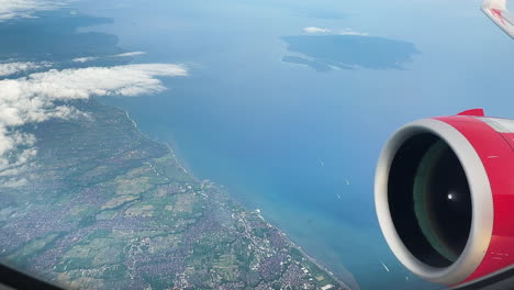 a sweeping view from an airplane window reveals bali’s coastline, lush inland, and the vast ocean beyond, capturing motion, altitude, and a sense of tropical arrival.