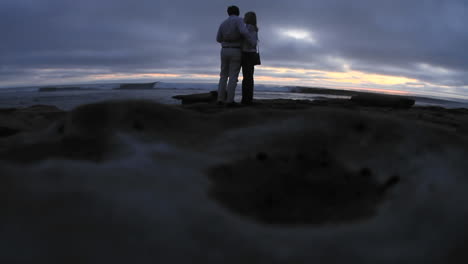 Ein-Paar-Sehen-Zu,-Wie-Die-Wellen-Kurz-Nach-Sonnenuntergang-Auf-Einen-Strand-Rollen-1