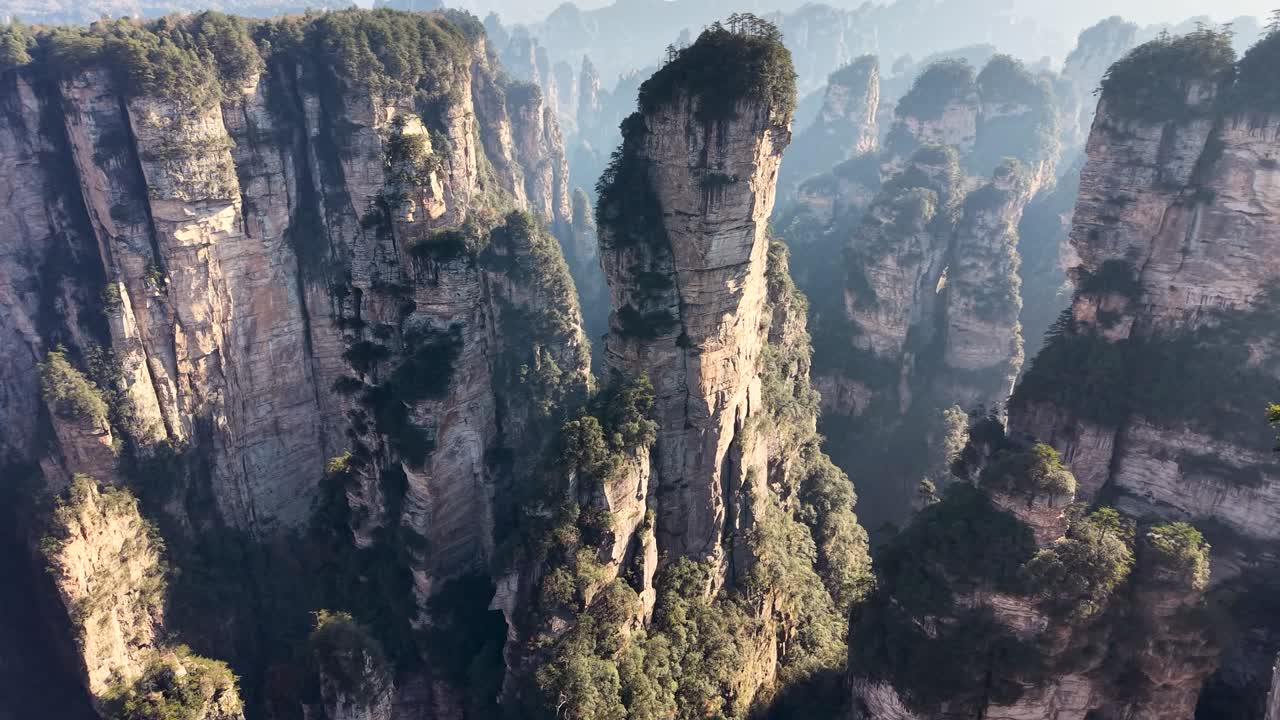 High aerial shot of unique mountain peaks covered in trees and morning fog in China