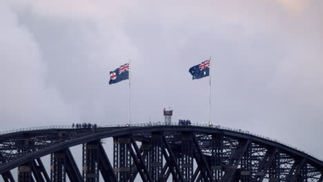 australian and new south wales flag waving in the wind with climbers on the sydney harbour bridge in australia