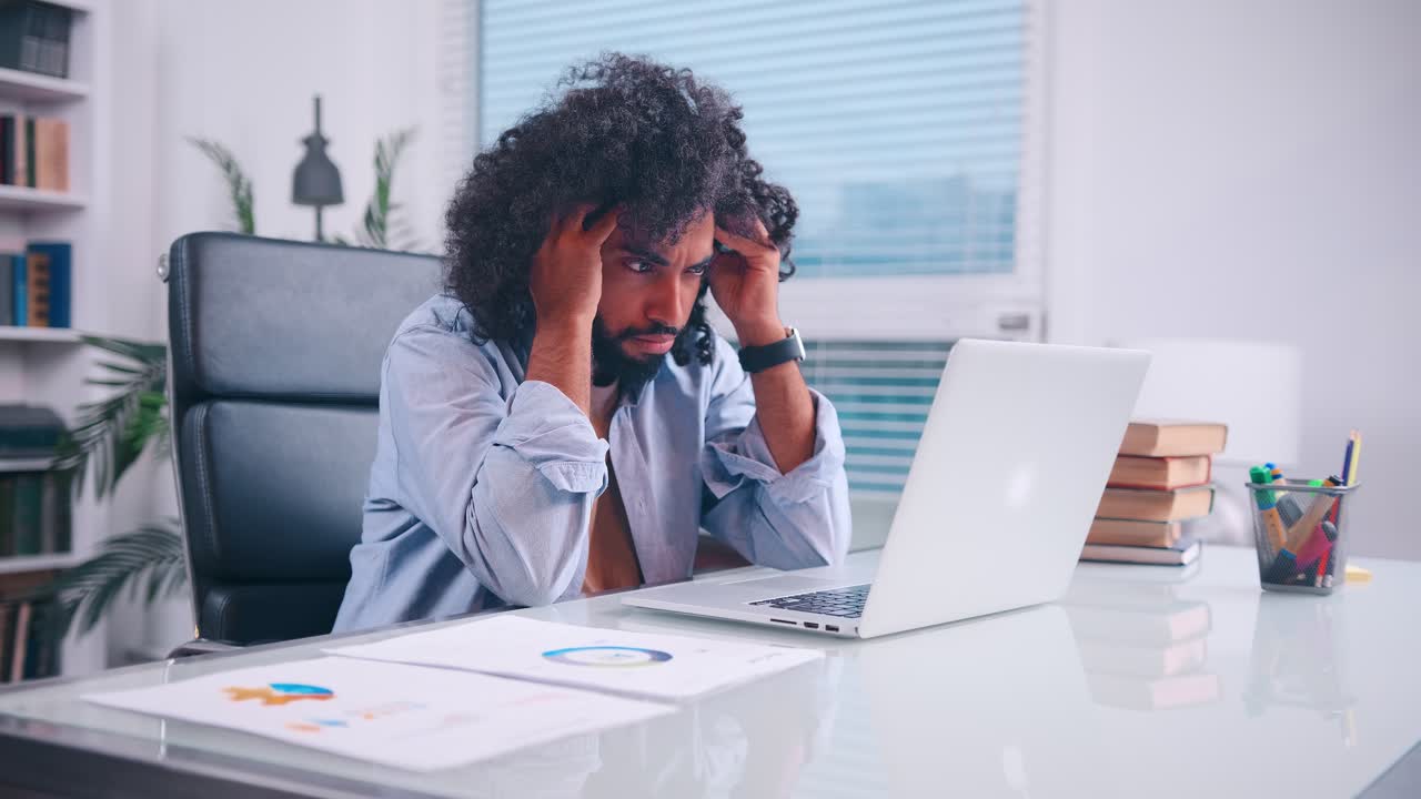 Tired middle eastern man clutches his head while sitting in his office