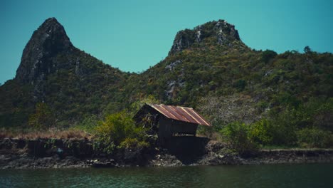 Una-Pequeña-Cabaña-Rota-Junto-A-Un-Río-En-Tailandia-Con-Colinas-De-Piedra-Caliza-Al-Fondo