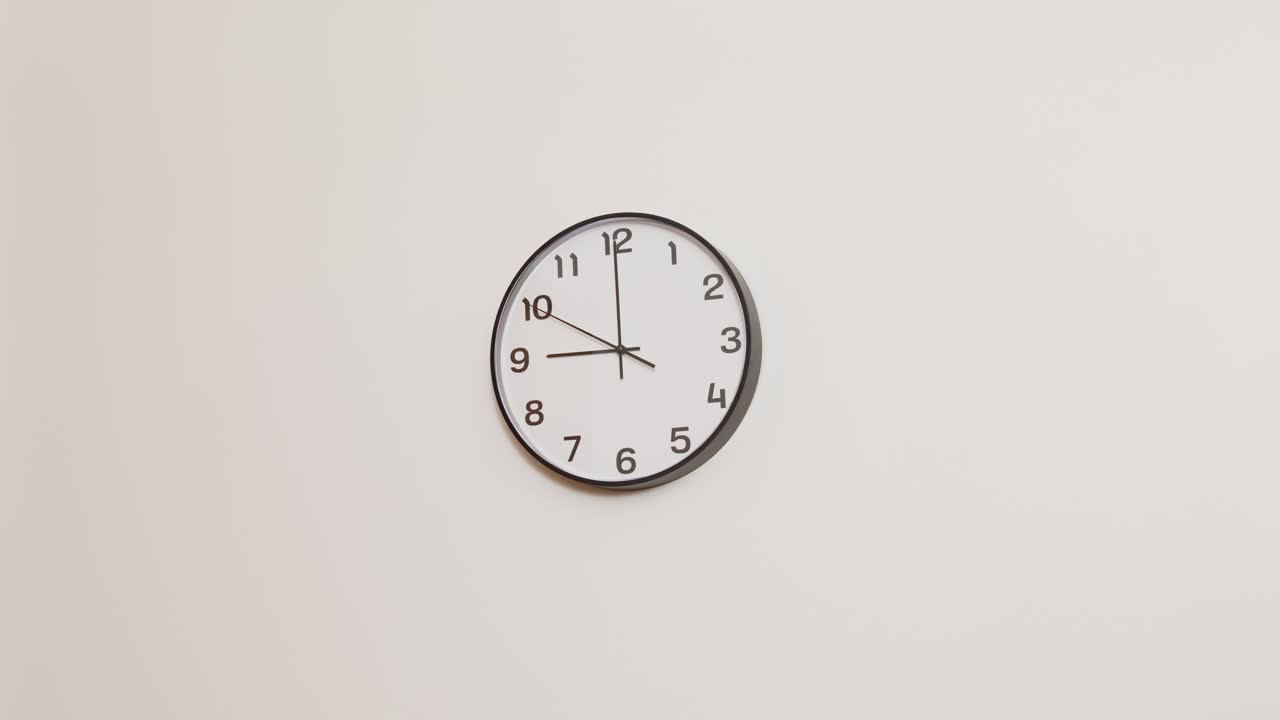 A minimalist wide shot of a black and white wall clock against a white background, showing the time at 9:00.