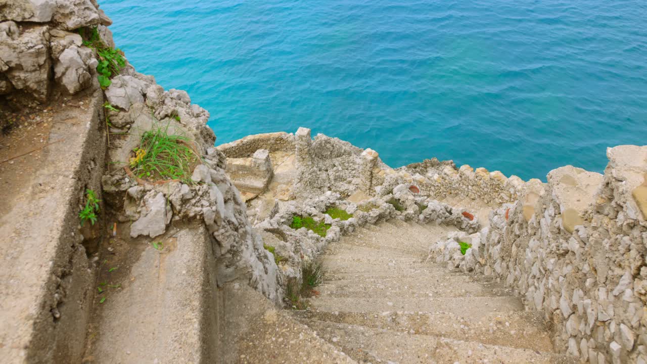 Top view of stone steps heading towards rocky and rugged shore with turquoise water during daytime.