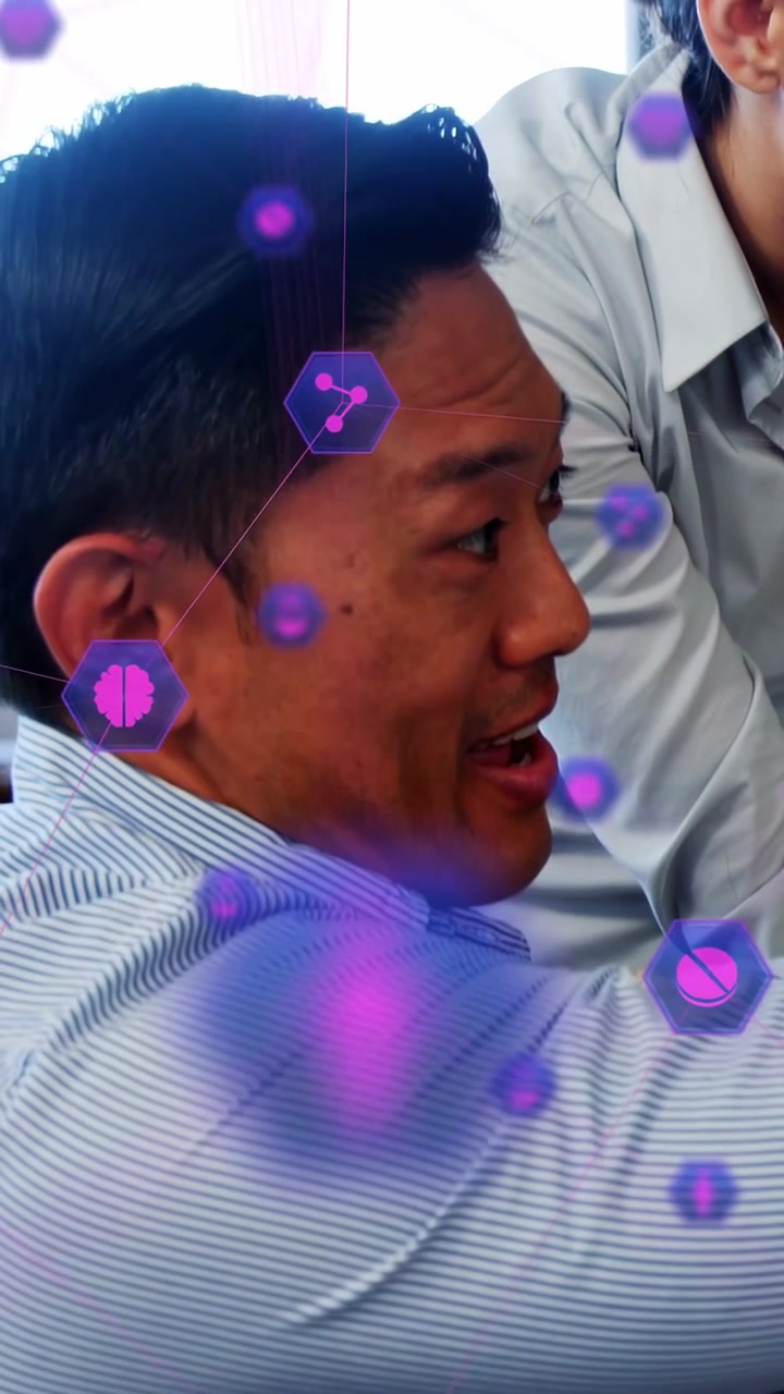 Vertical video: Seated man pointing at desk, explaining while purple AR hexes moving over office