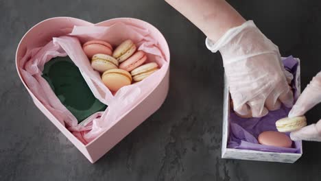 las manos femeninas ponen macarrones en la caja de regalos en la cocina, vista superior