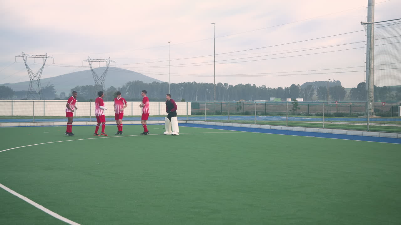 Playing field hockey, male team practicing on outdoor field with coach