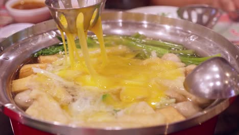 drizzling some scrambled eggs over a mixture of mushrooms and vegetables in a boiling and steamy hotpot, inside a restaurant in bangkok, thailand