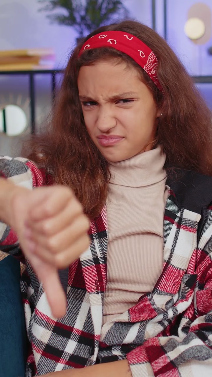 Upset young girl showing thumbs down dislike bad work disapproval dissatisfied feedback at home