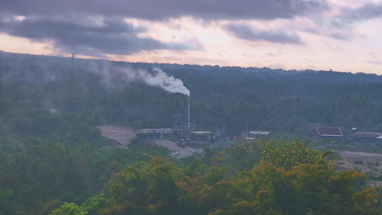 vista oscura, nublada y sombría de una fábrica con una chimenea humeante en medio de la naturaleza verde