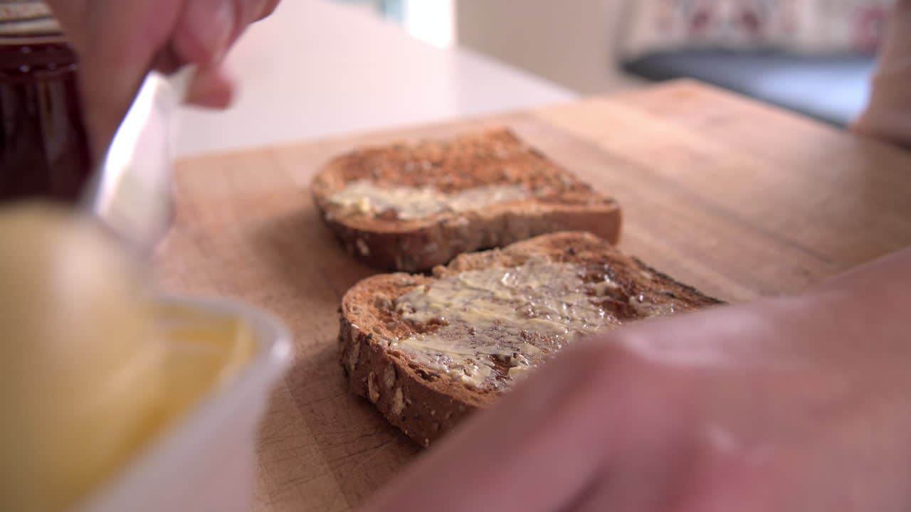 Person Spreading Butter And Jam Onto Slice Of Toast