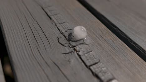 time lapse of an ice cube melting on wooden table, laying in the sun