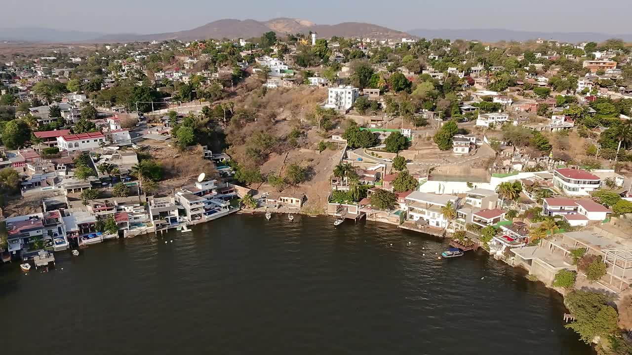 Drone aerial pan right view of lakeside houses, docks, boats and dry vegetation at Laguna Tequesquitengo, Morelos, Mexico