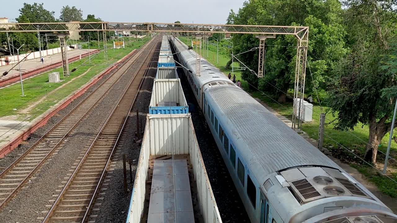 View from the top of open cargo train running on rail tracks in India, motion of train across countryside.