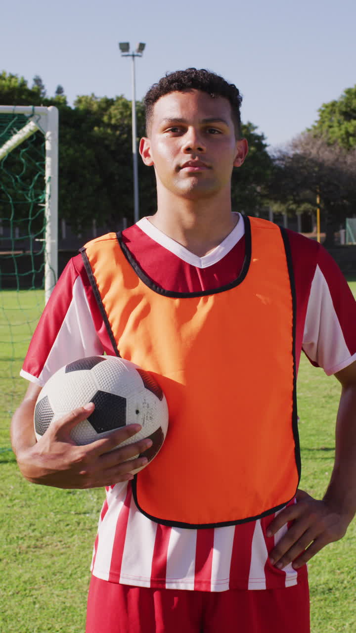 Vertical video of biracial football player on field kicking ball