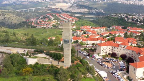 aerial view of a residential neighborhood featuring a tall concrete tower amidst red-roofed houses and green hills