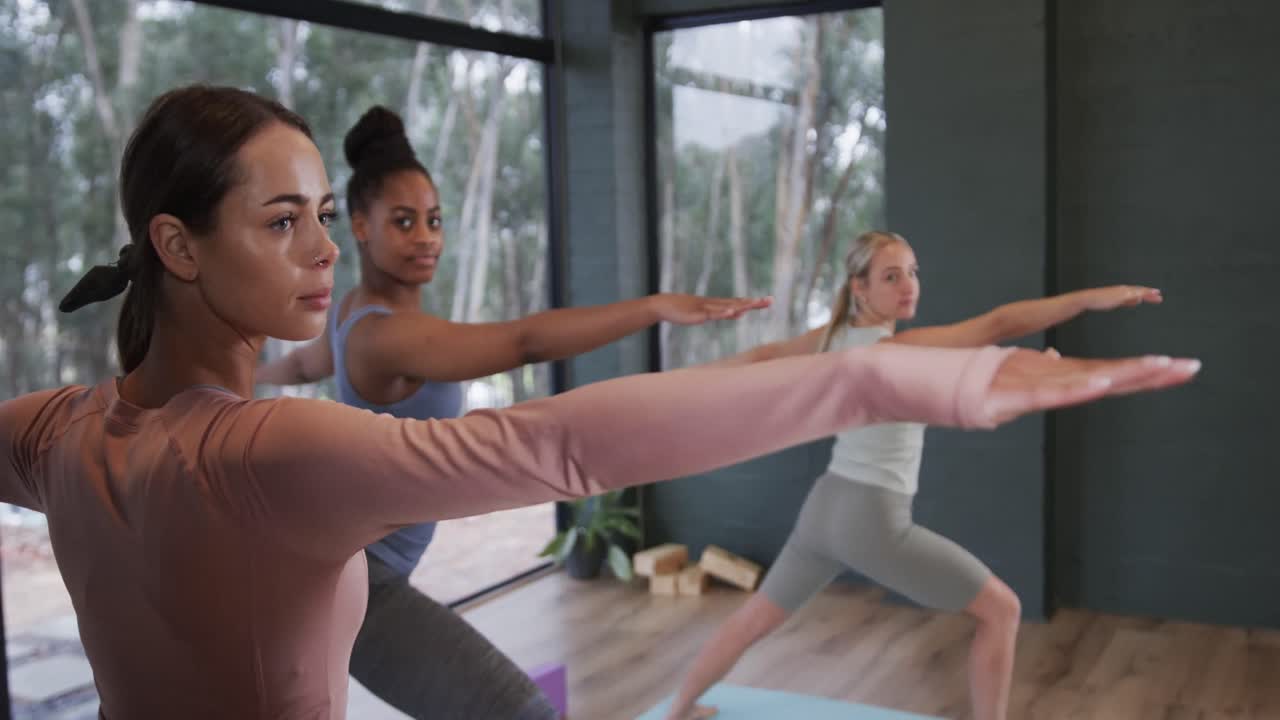 Donne diverse e concentrate che si allungano insieme sui tappetini in una lezione di yoga con l'istruttrice, al rallentatore