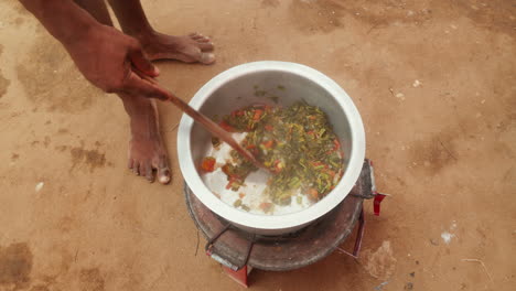 stirring a traditional stew in a large pot outdoors