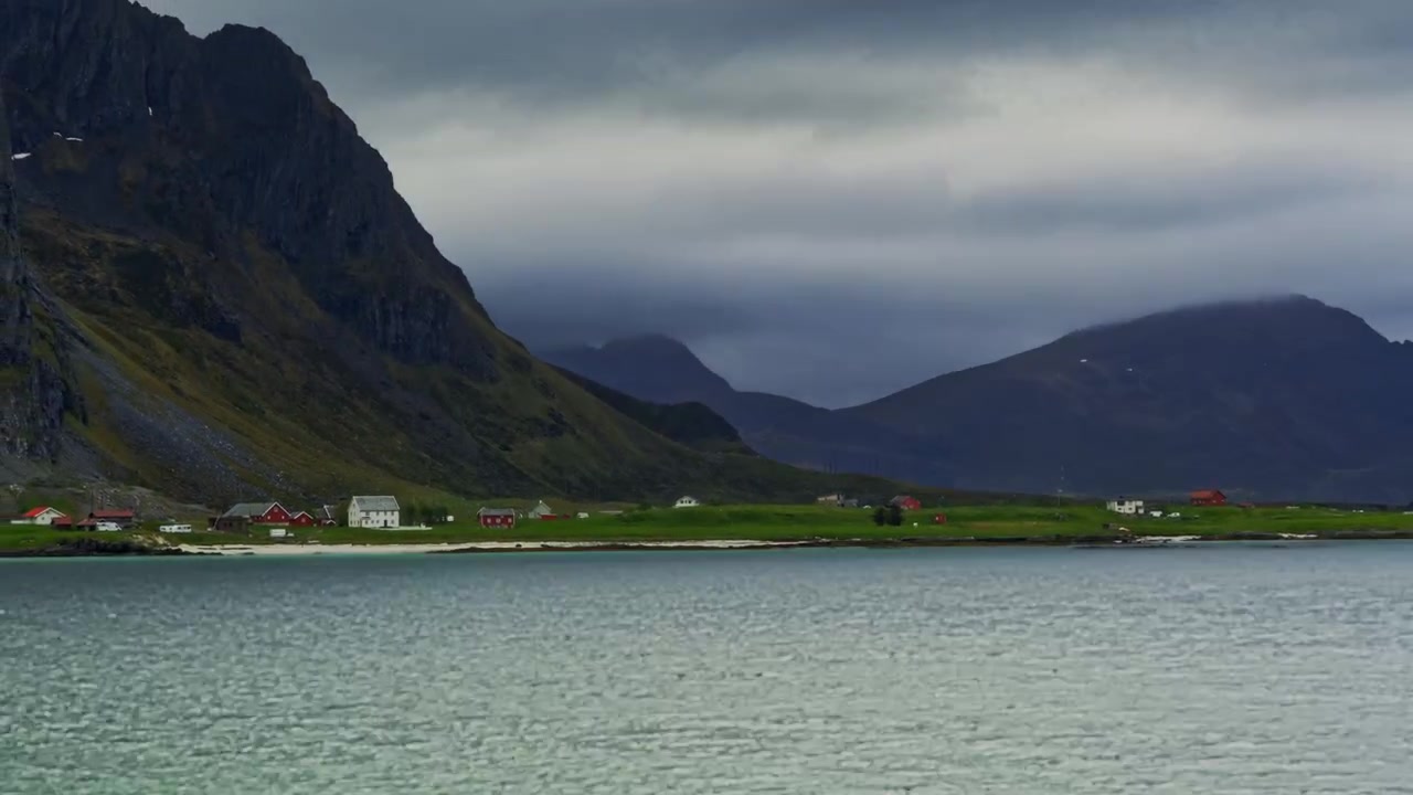 Zware regenwolken trekken over een kleine nederzetting aan zee, omringd door bergen. Een winderige, regenachtige dag met dramatisch wisselend licht in mei. Time-lapse, Lofoten, Noord-Noorwegen.