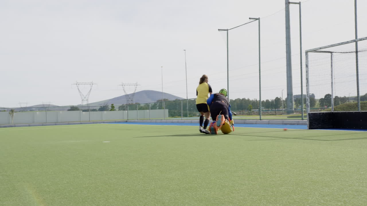 Goalkeeper in protective gear defending goal during intense field hockey match