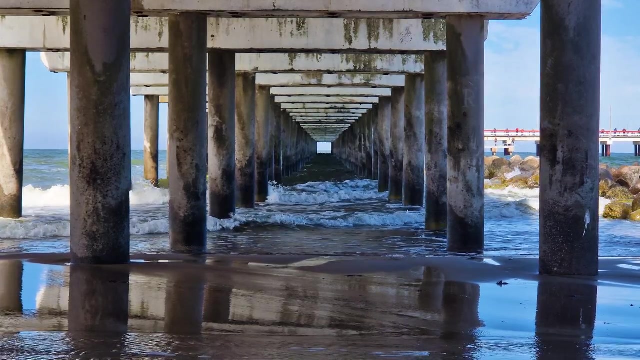 Underneath bridge, Baltic Sea waves reflecting blue sky and concrete pillars.