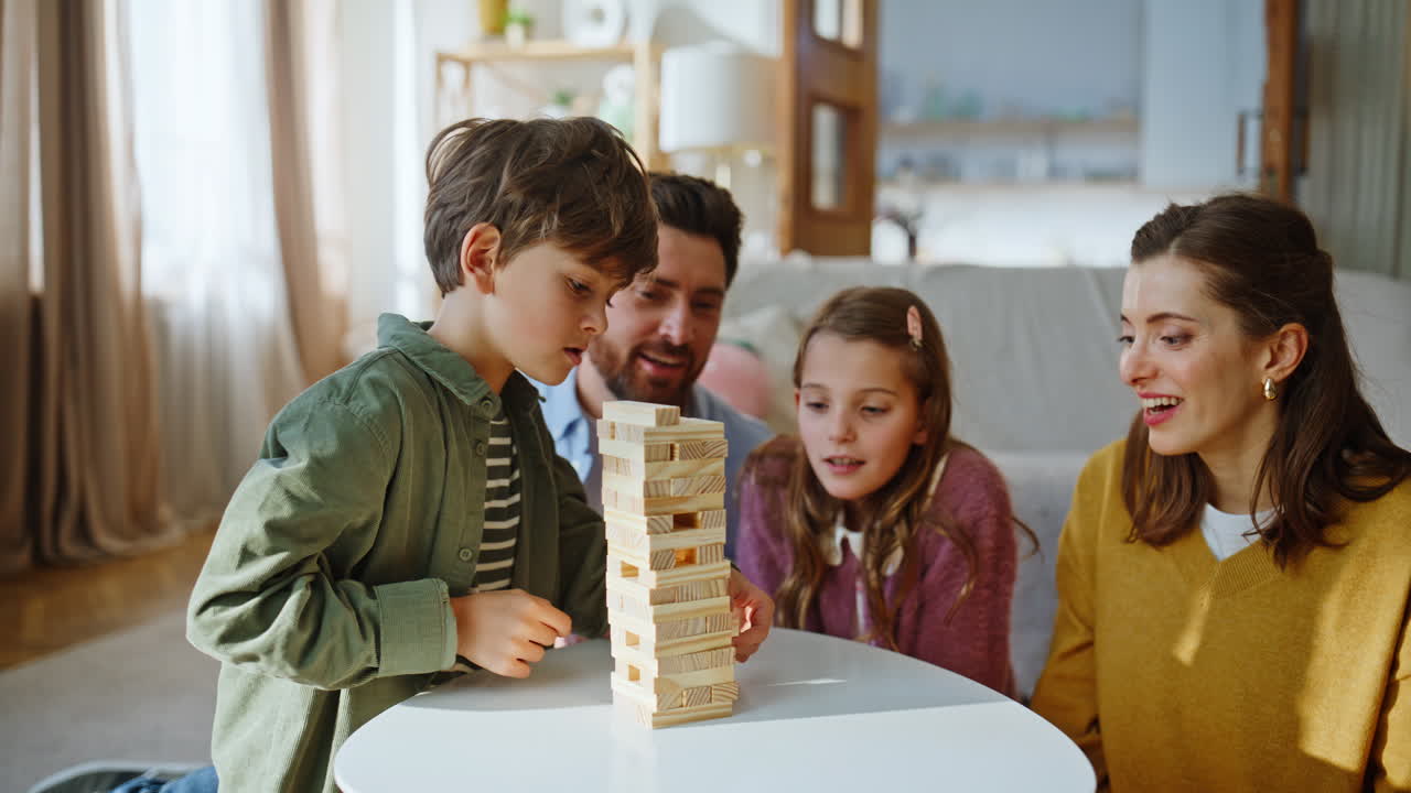 Primo piano di quattro membri di una famiglia che giocano a Jenga in soggiorno. Un bambino impila la torre