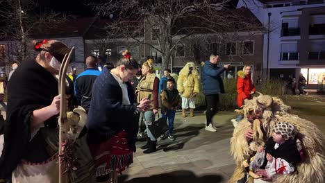 girls in traditional folk costumes take photos of a little boy on the lap of a local dressed in an animal costume at the busó-walking festival at night in mohacs, hungary.
