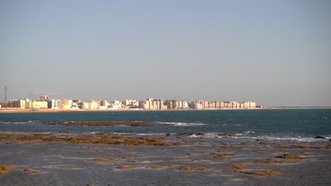 Océano-De-Marea-Baja-Con-Olas-Rompiendo-Y-Ciudad-Blanca-En-La-Distancia