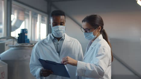 dos tecnólogos con abrigos de laboratorio y máscara en la planta de la fábrica