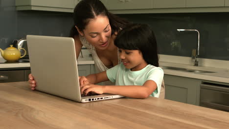 happy mother and daughter using laptop in the kitchen